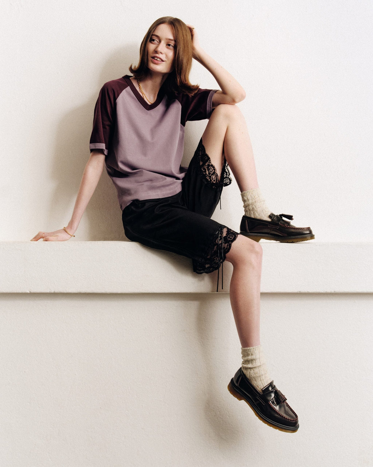 Mujer con remera ranglan lila, shorts negros con encaje y mocasines Dr. Martens con borla
